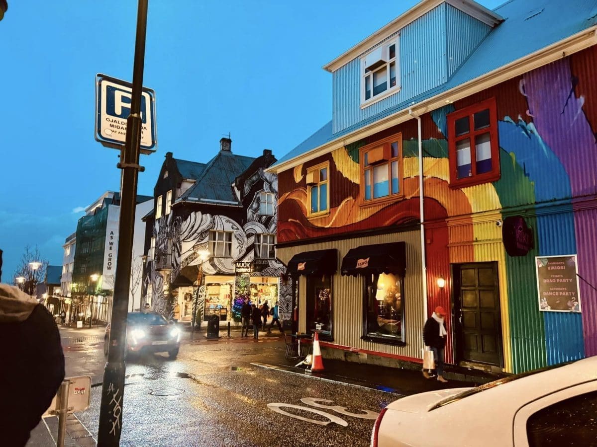 A street view of downtown Reykjavik featuring a colorful rainbow-painted building and a neighboring house covered in black and white artistic murals.