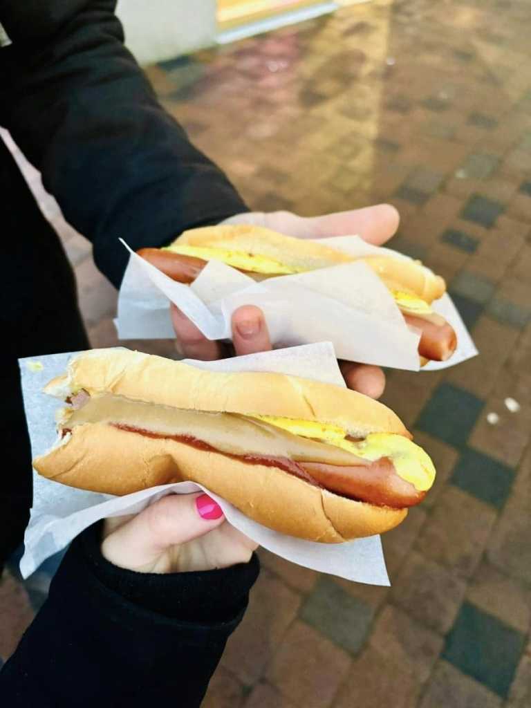 Two Icelandic hot dogs in white paper trays, topped with a generous swirl of brown mustard and creamy remoulade, sitting on a stainless steel counter at the famous Bæjarins Beztu Pylsur stand in Reykjavik.