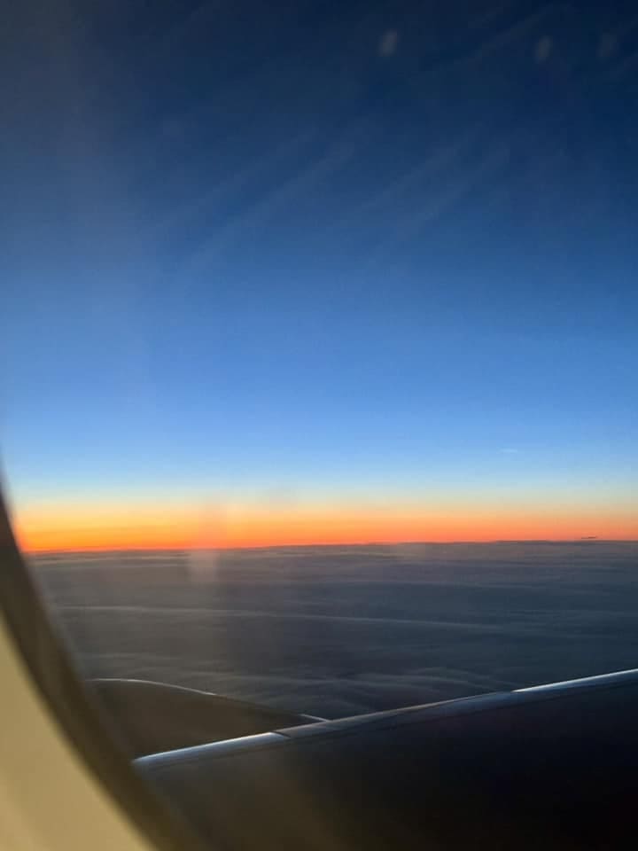 A view from an airplane window showing a brilliant orange and blue sunrise over a thick layer of clouds during a flight to Iceland.