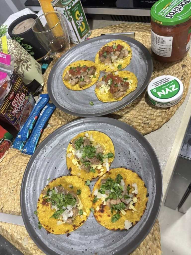 Two grey plates filled with authentic street tacos on yellow corn tortillas, topped with grilled meat, fresh onions, and cilantro. The plates are set on a woven placemat next to a jar of salsa and grocery supplies in a cozy Costa Rica Airbnb kitchen.